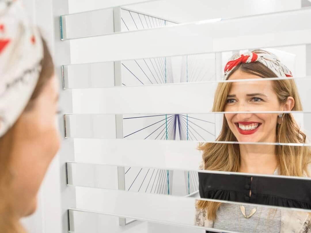 Two women are interacting with the Swap Noses exhibit at Museum of Illusions Atlanta. Parts of their faces alternate in mirror panels and empty spaces between them, forming a composite face of the women.