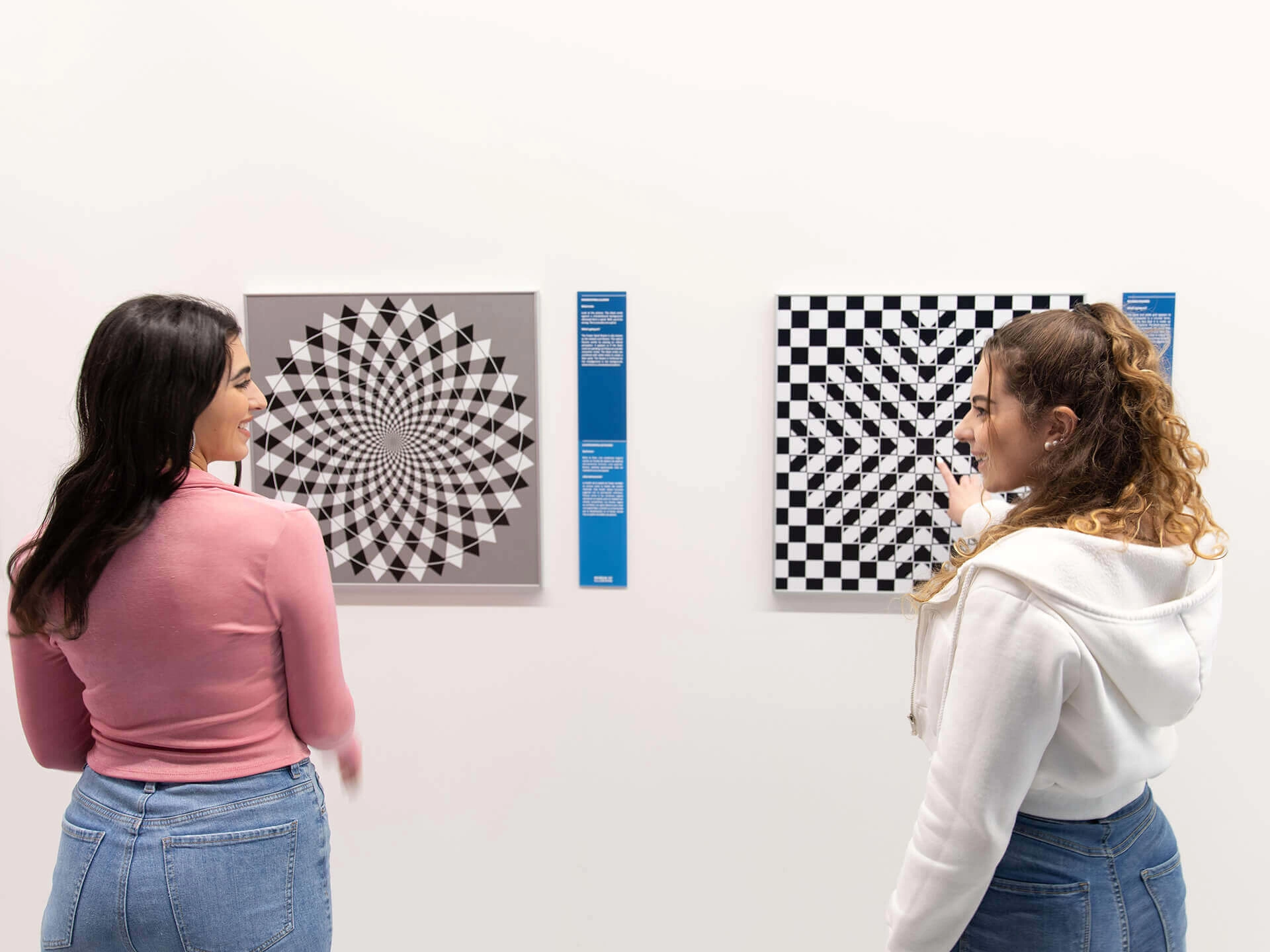 Two women are standing in front of the checkered optical illusions on the wall of the Museum of Illusions Atlanta.