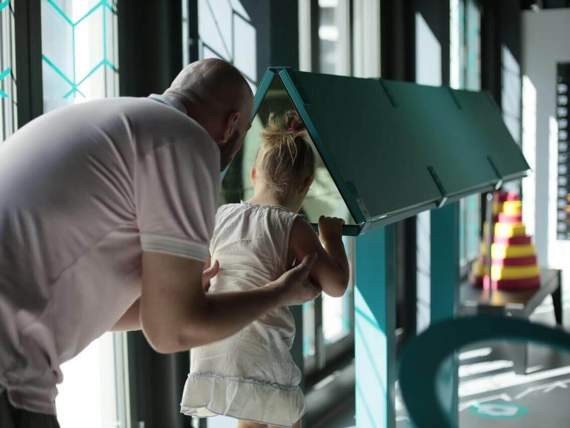 A man is lifting a little girl so that she can take a look in the Kaleidoscope exhibit at Museum of Illusions Atlanta.
