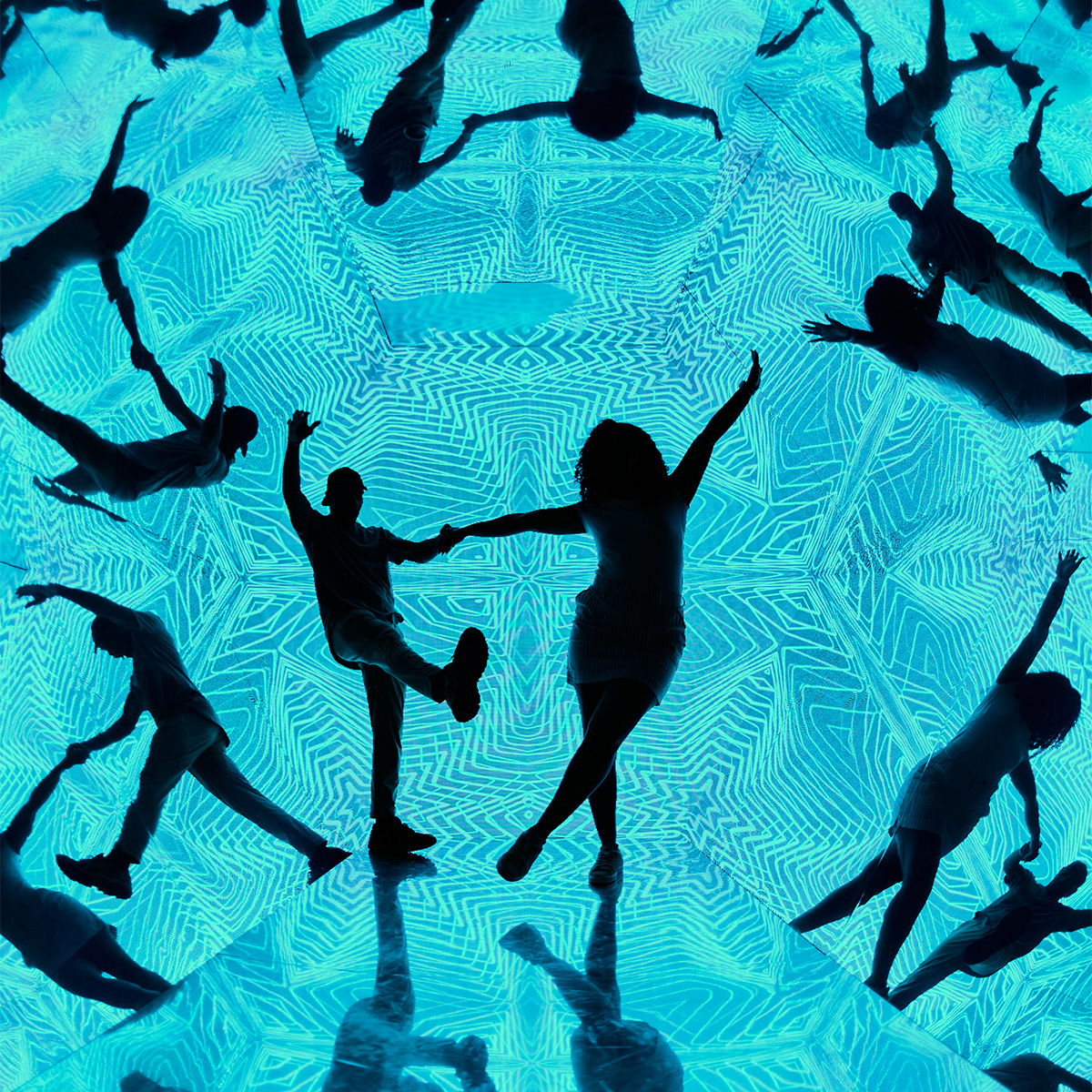 A man and a woman are dancing in the Walk in Kaleidoscope at Museum of Illusions Atlanta. They are surrounded by their reflections as well as the geometrical pattern of the exhibit.